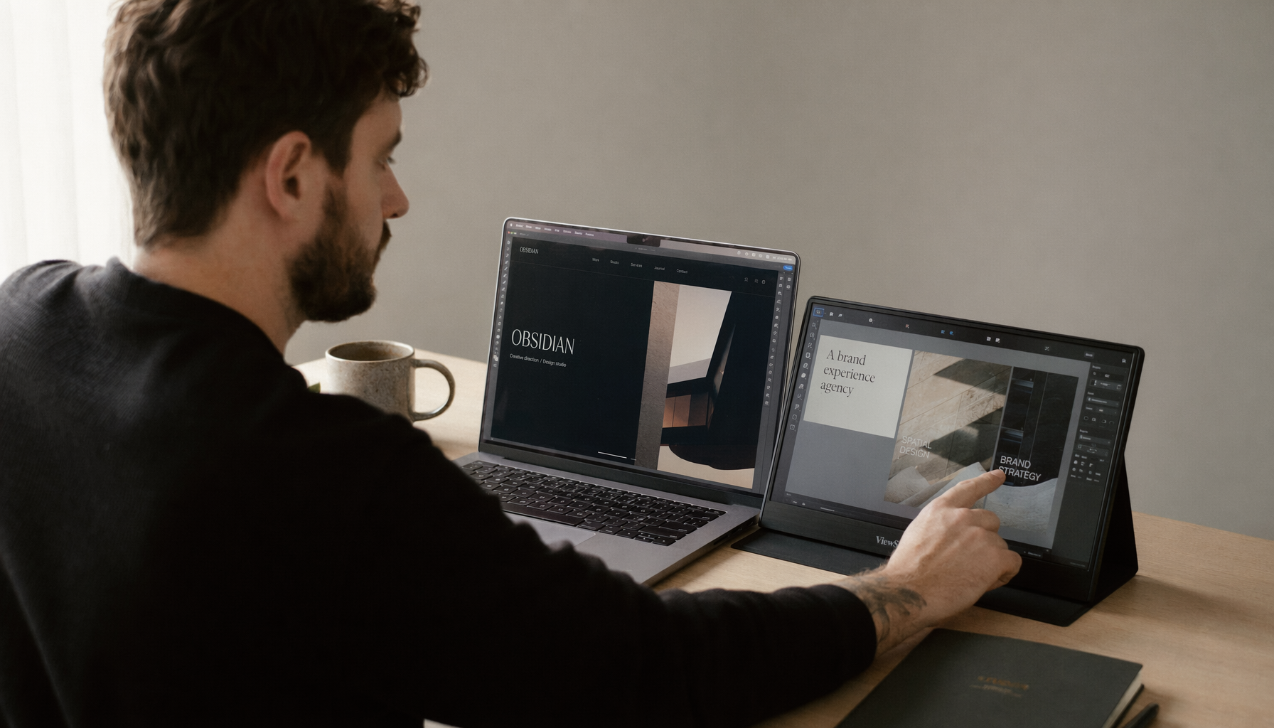 Designer using a touchscreen portable monitor alongside a non-touch laptop at a tidy home studio desk